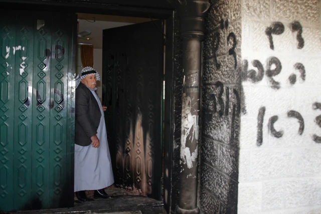 A Palestinian man stands near a door and wall of a mosque which were vandalised in the West Bank village of Deir Istiya, near the Jewish settlement of Ariel January 15, 2014. The mosque in the north of the West Bank was partly set on fire on Wednesday, in what Palestinians residents said was an attack by Jewish settlers living nearby. The main gate of the mosque and some of the carpeting inside were charred by the flames. Graffiti in Hebrew, reading "Revenge for spilled blood" and "Arabs Out", was scrawled on an outside wall and a door. REUTERS/Abed Omar Qusini (WEST BANK - Tags: POLITICS CIVIL UNREST RELIGION)
