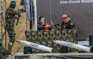 A member of the terror group Hamas and a representative of the Red Cross sign documents on stage next to the coffins of four Israeli hostages during their handover to the Red Cross in Khan Yunis. The transfer, part of a ceasefire deal, includes the remains of hostages believed to be members of the Bibas family.