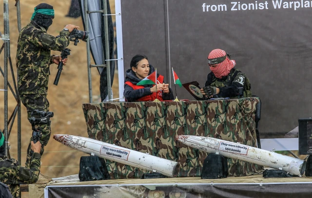 A member of the terror group Hamas and a representative of the Red Cross sign documents on stage next to the coffins of four Israeli hostages during their handover to the Red Cross in Khan Yunis. The transfer, part of a ceasefire deal, includes the remains of hostages believed to be members of the Bibas family.