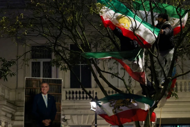 Demonstrators stand on tree branches displaying "Lion and Sun" pre-Iranian Revolution national flags outside the Iranian embassy during a rally in support of nationwide protests in Iran, in London, Britain, January 11, 2026.  Photo: Reuters Connect by Isabel Infantes