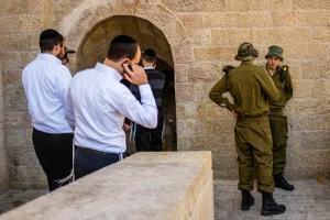 Ultra orthodox men make phone calls and walk out of the Hurva synagogue where soldiers stand in the background, in the jewish quarter of the Old City in Jerusalem on March 1, 2016. Photo by Corinna Kern/Flash90