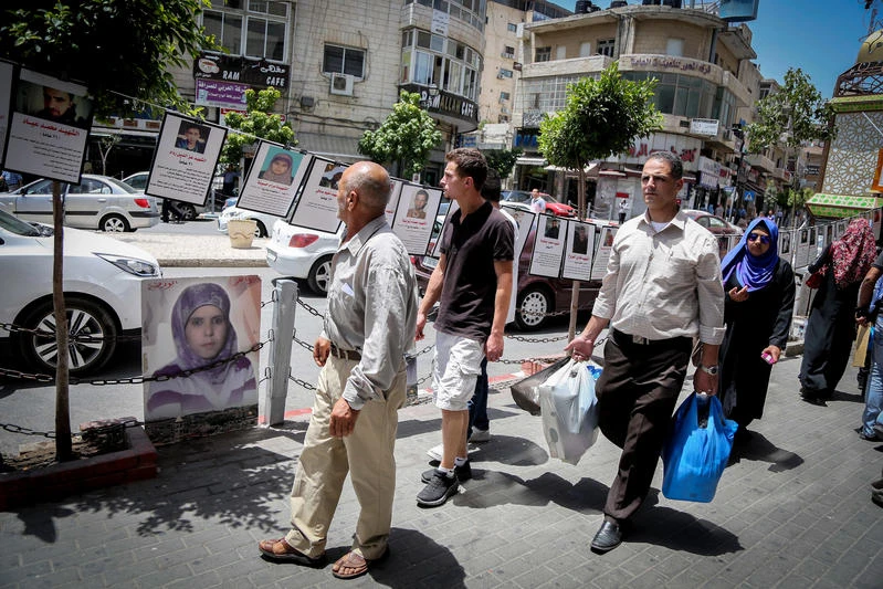 Palestinians walk past posters depicting Palestinian martyrs hanging on hte streets of the West Bank city of Ramallah, to show solidarity with them. June 13, 2016. Photo by FLASH90