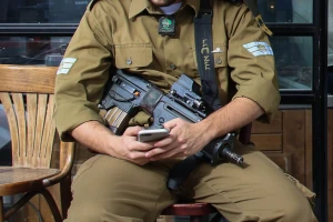 An IDF soldier sitting with his phone in front of a restaurant on Agripas street, on February 12, 2018. Photo by Liba Farkash/Flash90