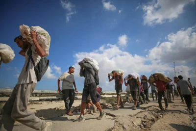 Displaced Palestinians carry food parcels and supplies from a GHF aid distribution point at the “Netzarim corridor” in the central Gaza, August 5, 2025. Photo by Ali Hassan/Flash90