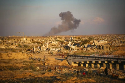 Palestinians walk in the street as smoke rises following an Israeli airstrike in Gaza City, December 2, 2025. Photo by Ali Hassan/Flash90