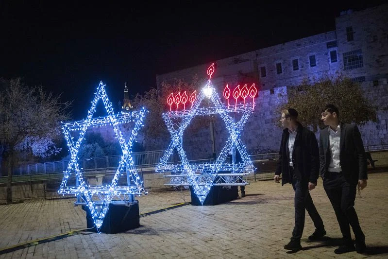 People walk next to a Menorah (Hanukkah lamp) in a shape of a david star ahead of the Jewish holiday of Hanukkah, outside Jerusalem's Old City, December 13, 2025. Photo by Chaim Goldberg/Flash90
