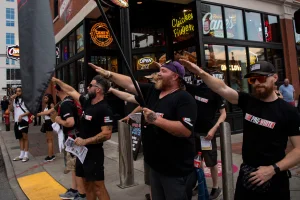 Members of the Goyim Defense League – wearing shirts with the words “Pro White” on the front and “Whites Against Replacement” on the back – make Nazi salutes as flags displaying swastikas are held by other members of the group on Lower Broadway in Downtown Nashville, Tenn., Sunday, July 14, 2024.