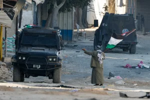 A man holding a Palestinian flag gestures next to a vehicle of Palestinian security forces amid clashes with militants at the camp, in Jenin, northern Samaria, December 14, 2024. REUTERS/Raneen Sawafta