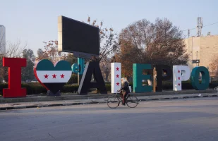 A man on a bicycle passes by a sign reading "I love Aleppo," adorned with flags representing the new Syrian opposition, in Aleppo, Syria, January 8, 2025. REUTERS/Karam al-Masri