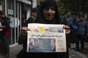 A veiled Iranian woman holds a newspaper featuring portraits of Iranian Foreign Minister Abbas Araghchi and Steve Witkoff, White House special envoy, while she shows her protest against Iran and U.S. negotiations in downtown Tehran, Iran, on April 9, 2025. Photo via Reuters.