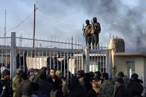Members of the Syrian government security forces stand guard as a group of detainees gather at al-Hol camp after the government took control of it following the withdrawal of Syrian Democratic Forces (SDF), in Hasaka, Syria, January 21, 2026. Photo: Reuters Connect by Khalil Ashawi