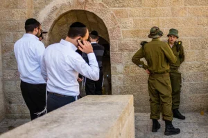 Ultra orthodox men make phone calls and walk out of the Hurva synagogue where soldiers stand in the background, in the jewish quarter of the Old City in Jerusalem on March 1, 2016. Photo by Corinna Kern/Flash90