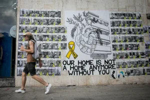Israelis walk past a mural photographs of Israelis held hostage by Hamas terrorists in Gaza since the October 7 massacre, on Dizengoff in Tel Aviv. The mural was designed by street artists Hastickeriot and Yiddish Feminist. June 23, 2024 (Photo by Miriam Alster/FLASH90).