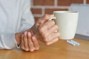 Illustration: Close-up of an elderly woman steadying her hand while drinking, illustrating symptoms associated with Parkinson’s disease. Photo: Shutterstock
