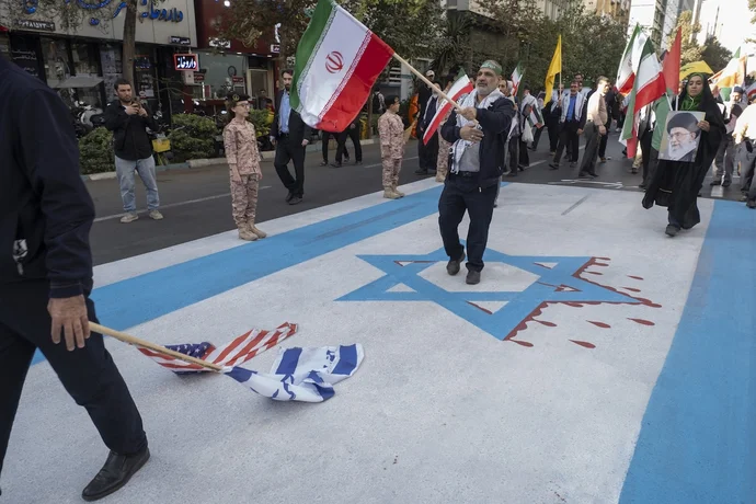 An Iranian man drags the U.S. and Israeli flags along a giant Israeli flag during an anti-American and anti-Israeli rally