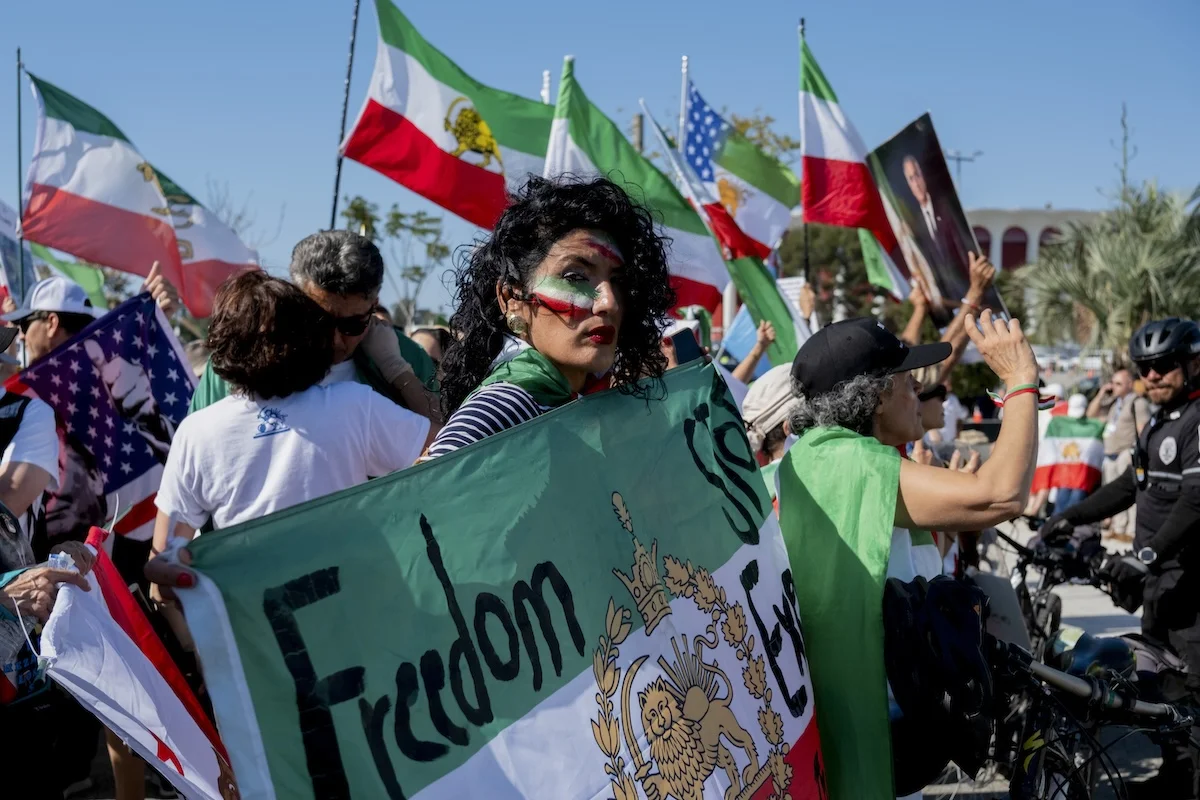 A protester with face paint holds a pre-revolutionary Iranian flag with the word 
