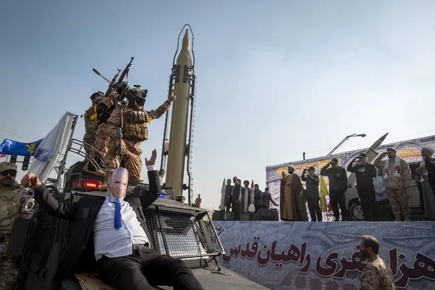 Commanders of the Islamic Revolutionary Guard Corps (IRGC) salute as an unidentified man wearing a mask featuring a portrait of Israeli Prime Minister Benjamin Netanyahu performs, while being carried by an IRGC anti-riot armored vehicle during a military rally in downtown Tehran, Iran, on January 10, 2025. (Photo by Morteza Nikoubazl/NurPhoto)