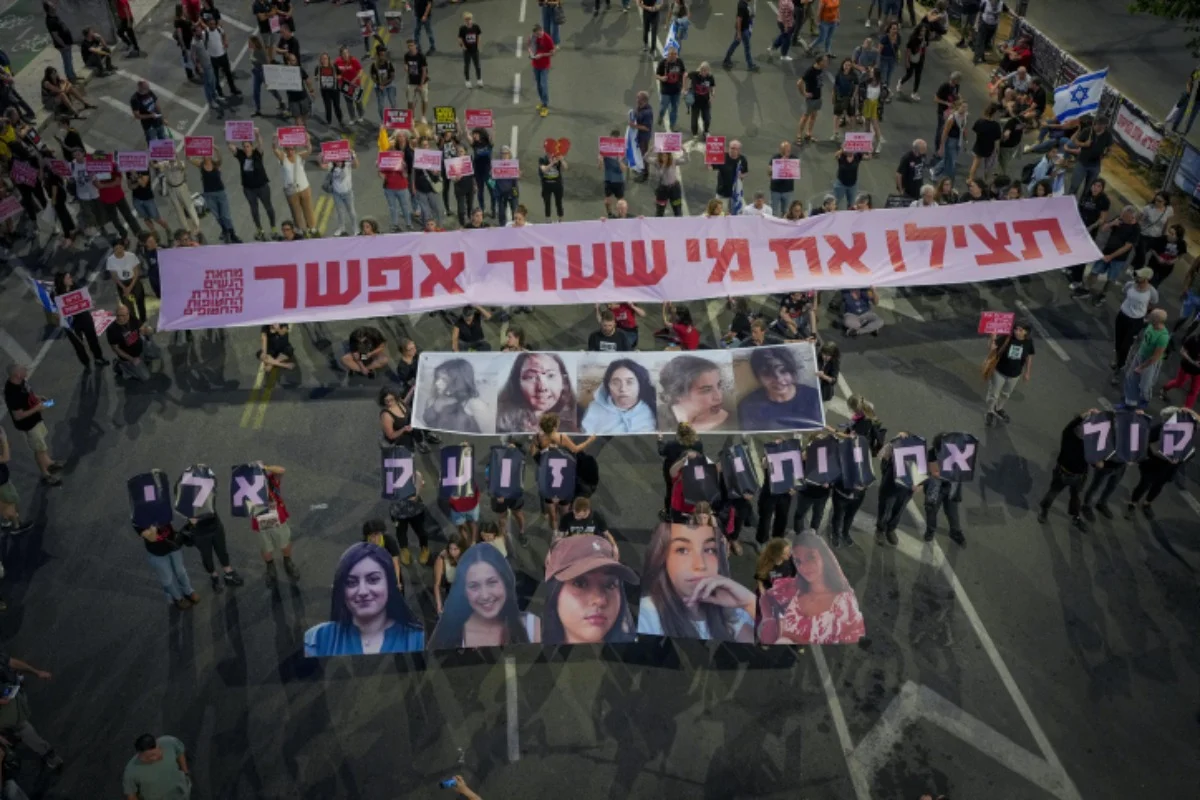 Demonstrators hold images of five female soldiers held hostage by Hamas terrorists in Gaza. The banner in Hebrew reads: 
