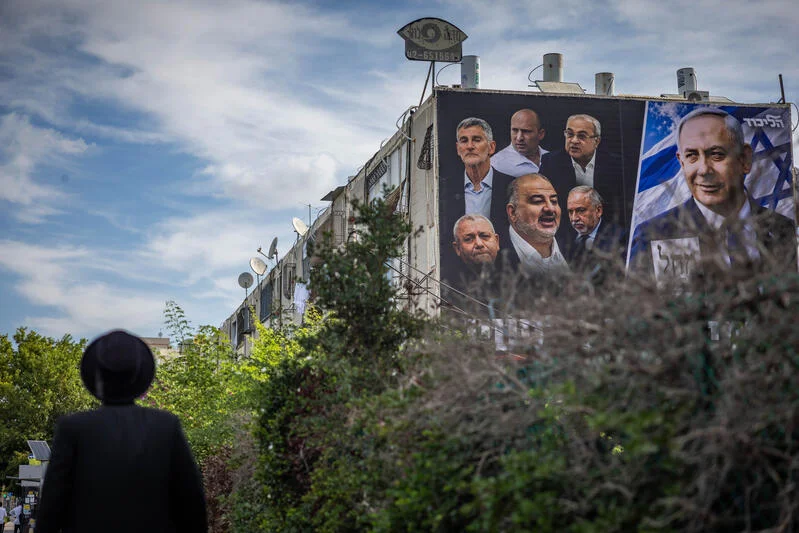 People walk past a giant election campaign poster displayed on a building in the southern Israeli city of Ashdod