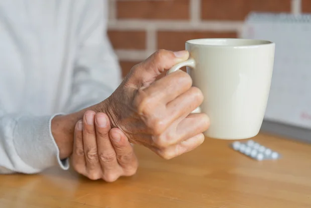 Illustration: Close-up of an elderly woman steadying her hand while drinking, illustrating symptoms associated with Parkinson’s disease. Photo: Shutterstock