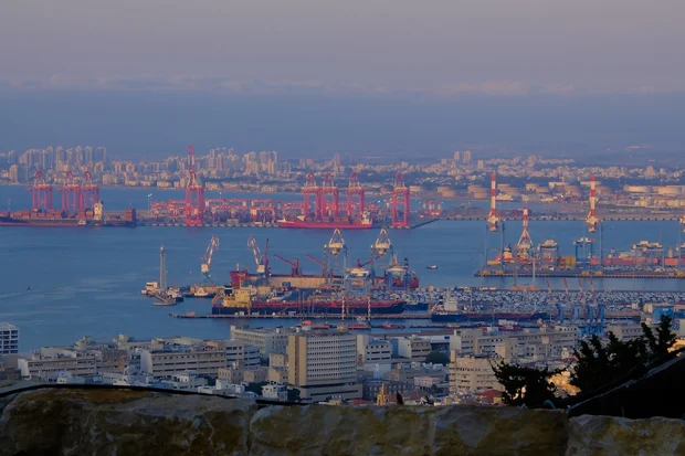 A panoramic view of the port of Haifa, Israel, with large cargo ships, cranes, and industrial buildings in the foreground and oil tanks in the background. (Photo: Shutterstock)